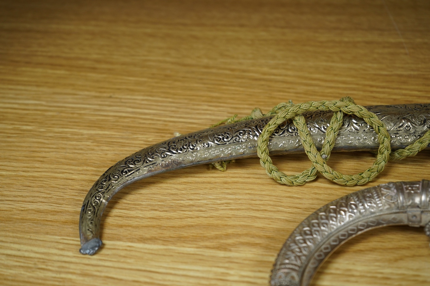 An Omani silver spice box in the form of a curved powder flask, together with a Moroccan dagger Jambiya with nickel hilt and sheath, both 20th century. Condition - fair.
